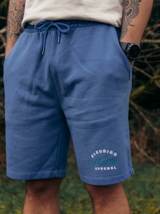 Person wearing blue shorts with a brand logo, standing outdoors.