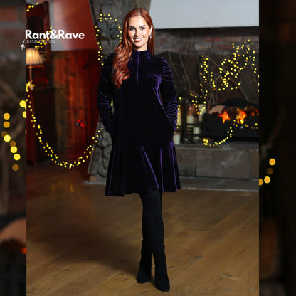 Woman in a purple velvet dress standing in a decorated room with lights and a fireplace.