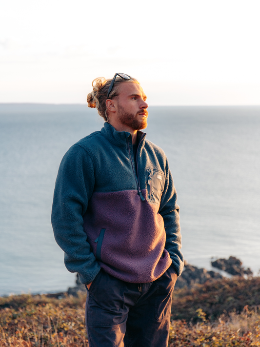 Men wearing two tone ziip up fleece standing on cliff with sea in the background