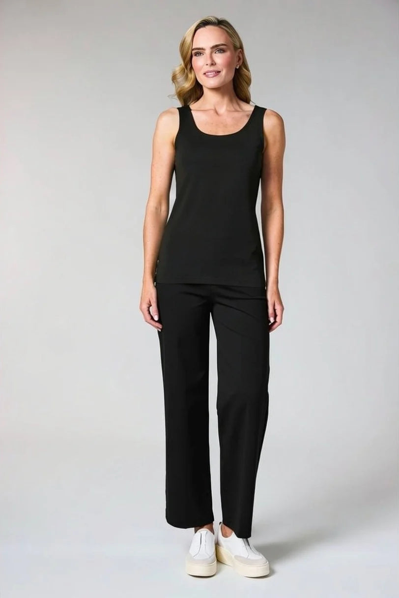 A woman modeling a black sleeveless scoop-neck tank top and matching black wide-leg trousers, paired with white sneakers, against a light gray studio background.