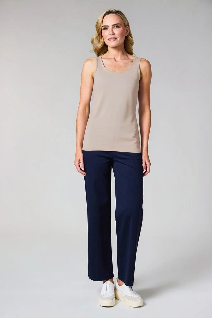 A woman modeling a sleeveless scoop-neck tank top in beige and navy blue cropped trousers, paired with white sneakers, against a light gray studio background.