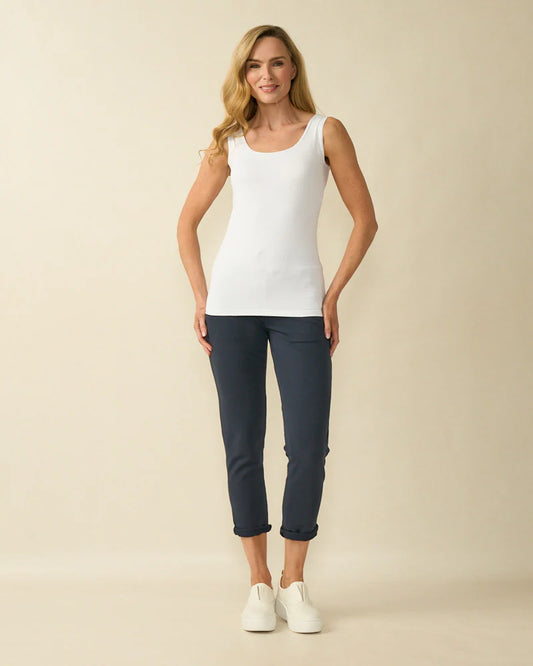 Woman wearing a white tank top and dark blue pants on a beige background