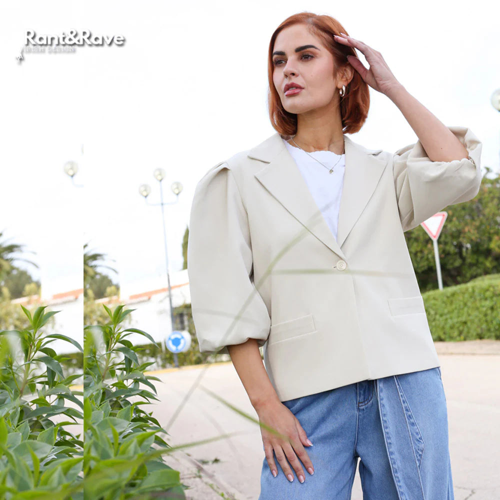 Woman wearing a beige blazer and blue jeans outdoors with 'Rant&Rave' branding.
