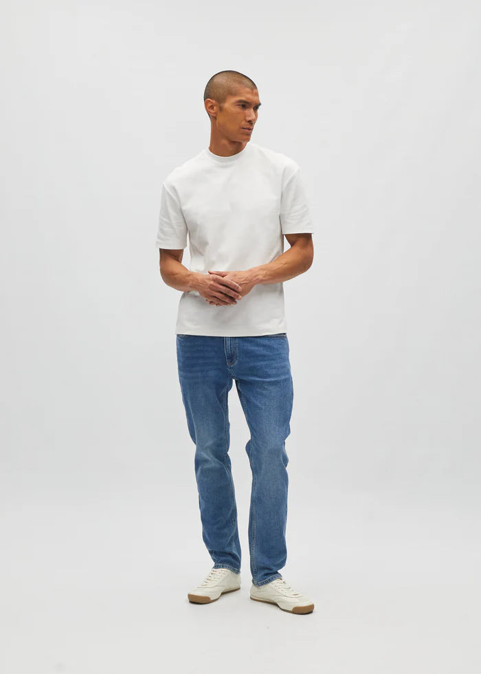 Man wearing a white t-shirt and blue jeans standing against a plain background