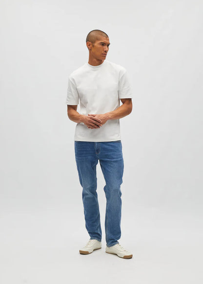 Man wearing a white t-shirt and blue jeans standing against a plain background
