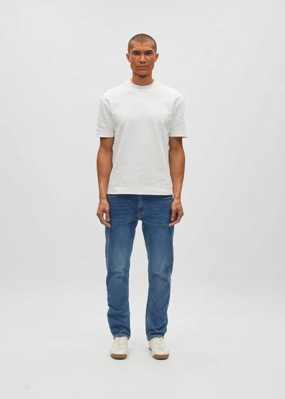 Man wearing a white t-shirt and blue jeans on a plain background