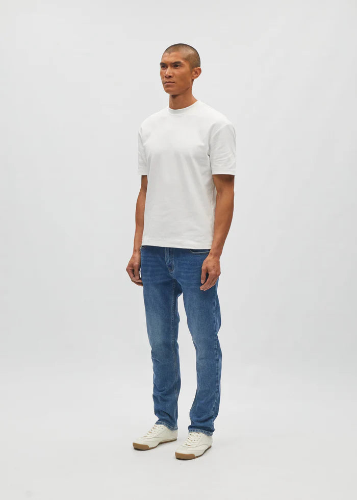 Man wearing a white t-shirt and blue jeans on a plain background