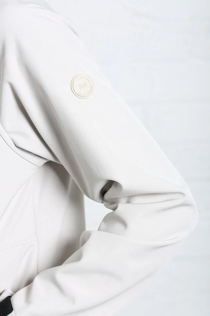 Close-up of a light gray or off-white jacket sleeve with a circular metallic emblem on the upper arm, set against a matching light gray background.