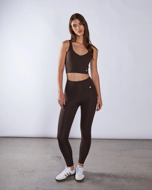 Woman wearing a brown athletic outfit with white sneakers on a plain background