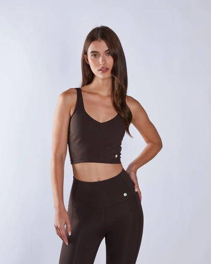 Woman wearing a brown sports bra and leggings on a light gray background