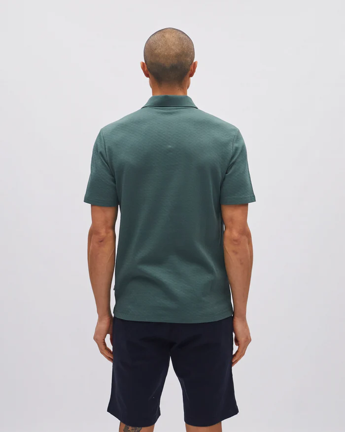 Man wearing a green polo shirt and dark shorts on a light gray background