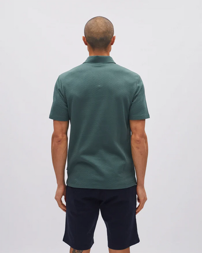 Man wearing a green polo shirt and dark shorts on a light gray background