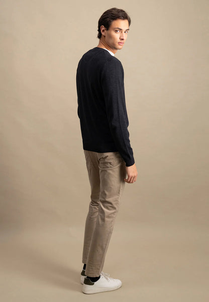 Man wearing a navy sweater and beige pants against a beige background