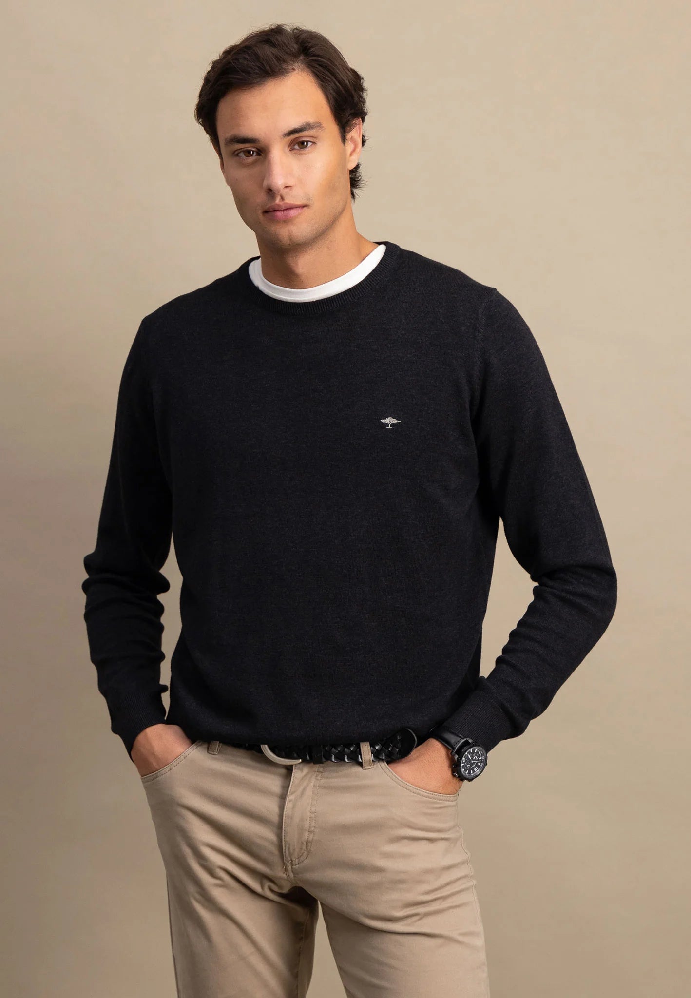 Man wearing a black sweater with a logo on a beige background