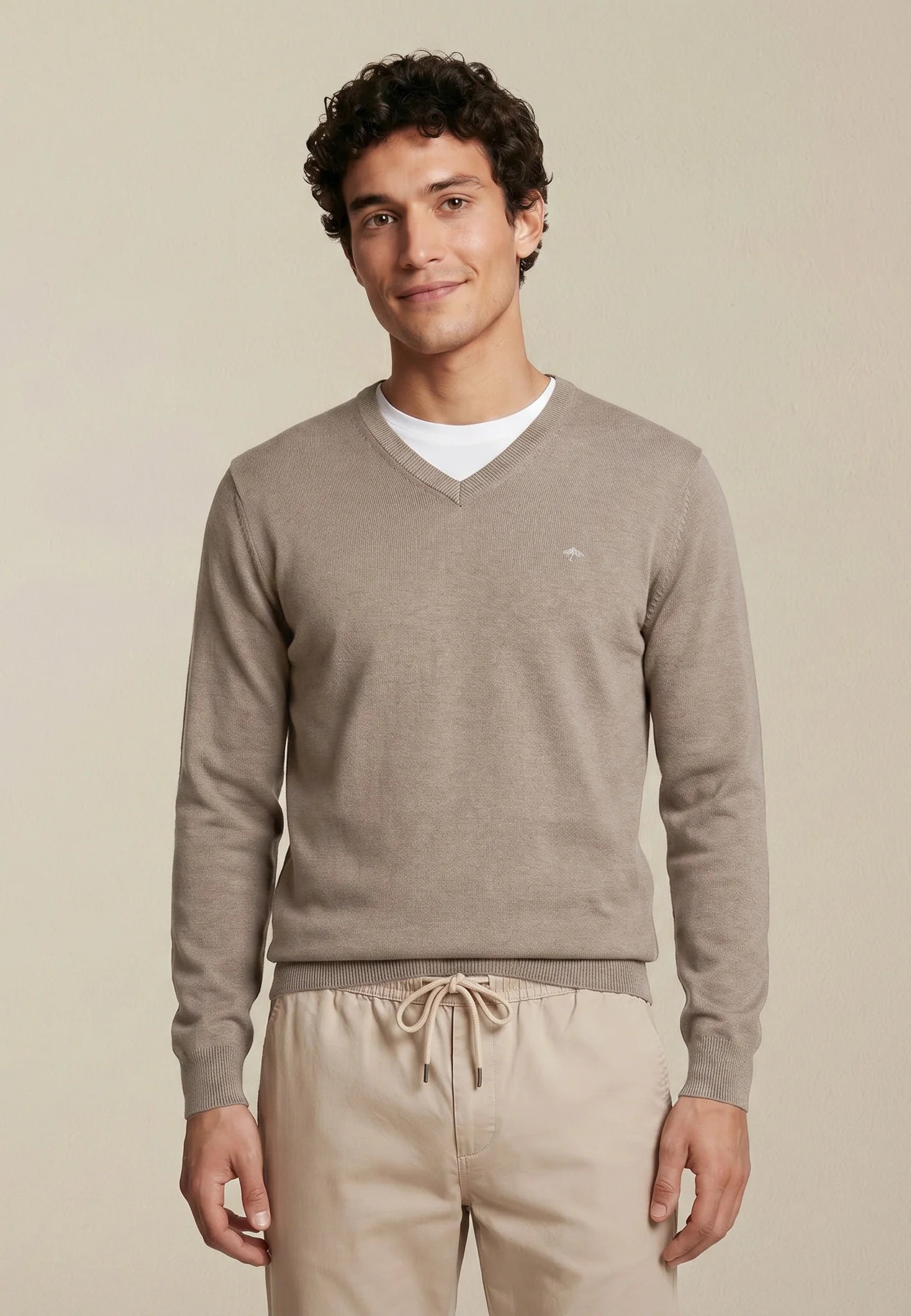 Man wearing a beige sweater and pants on a plain background