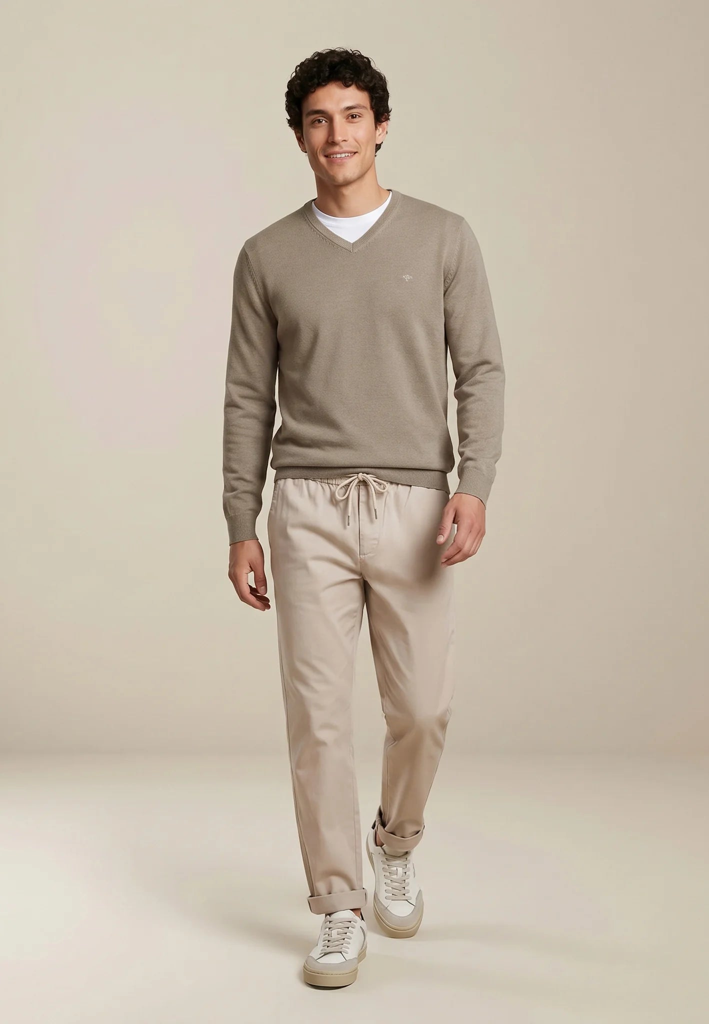Man wearing a beige sweater and pants on a plain background