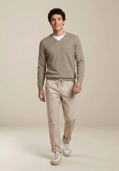 Man wearing a beige sweater and pants on a plain background