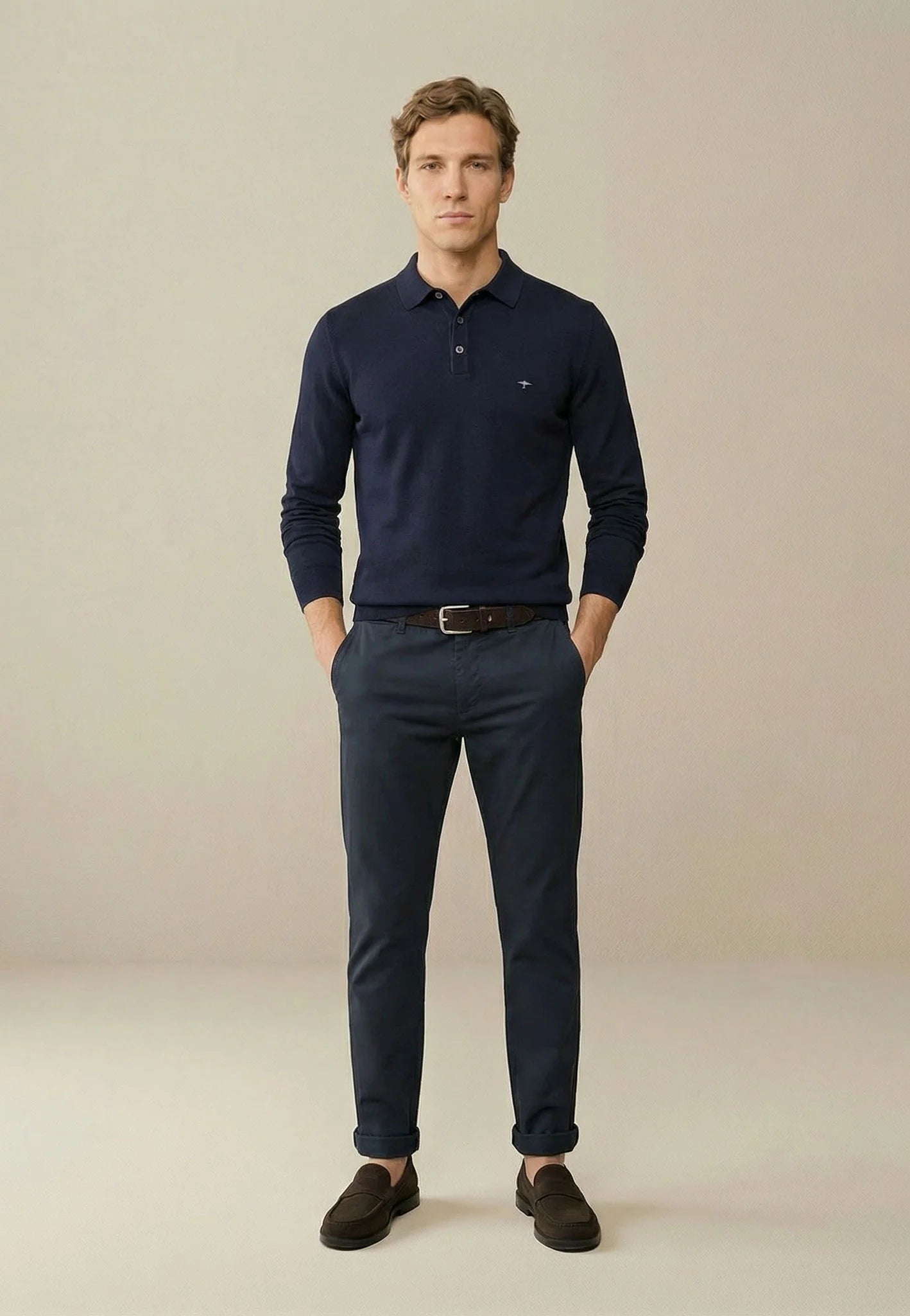 Man wearing a navy blue polo shirt and pants against a beige background