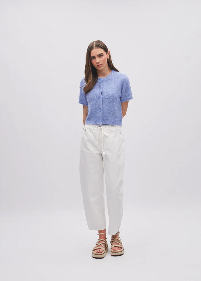 Woman wearing a blue top and white pants on a plain background