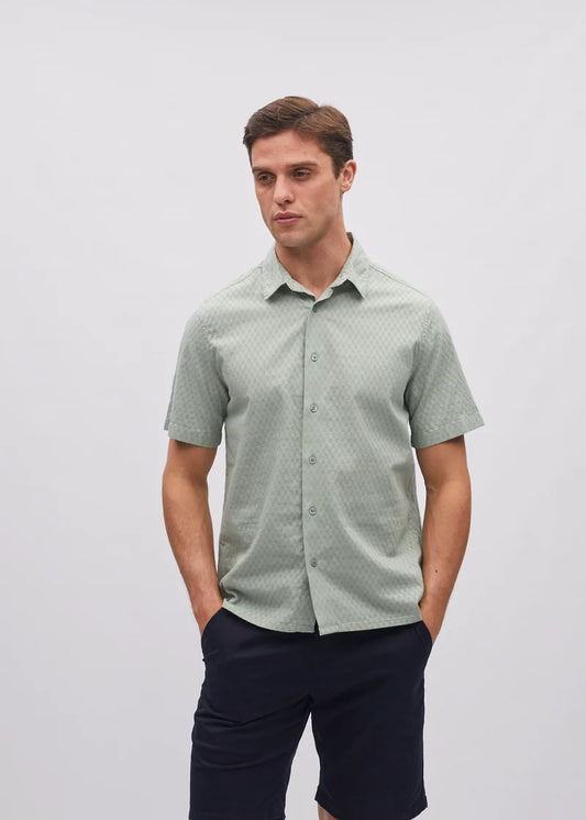Man wearing a green patterned shirt and dark pants on a light gray background