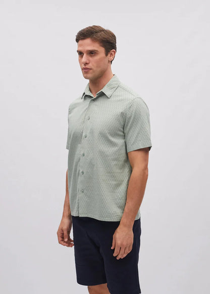 Man wearing a light green patterned shirt and dark shorts on a white background