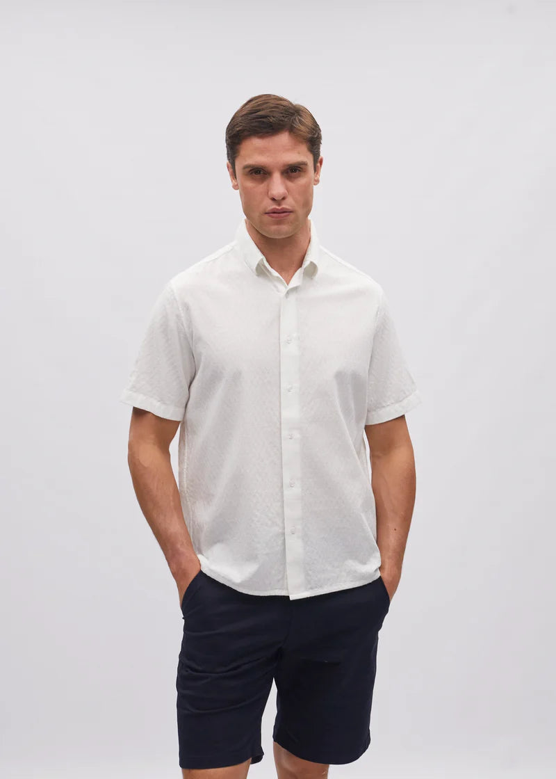 Man wearing a white short-sleeve shirt and navy shorts on a light gray background