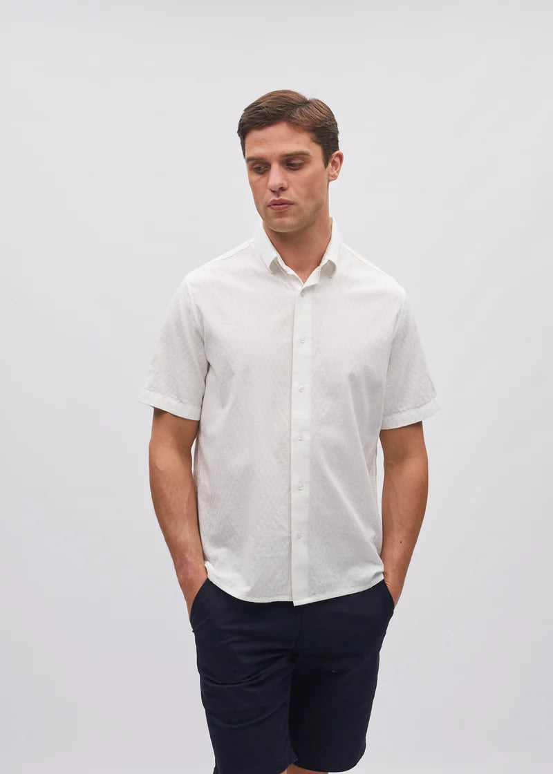 Man wearing a white short-sleeve shirt and navy pants on a light gray background