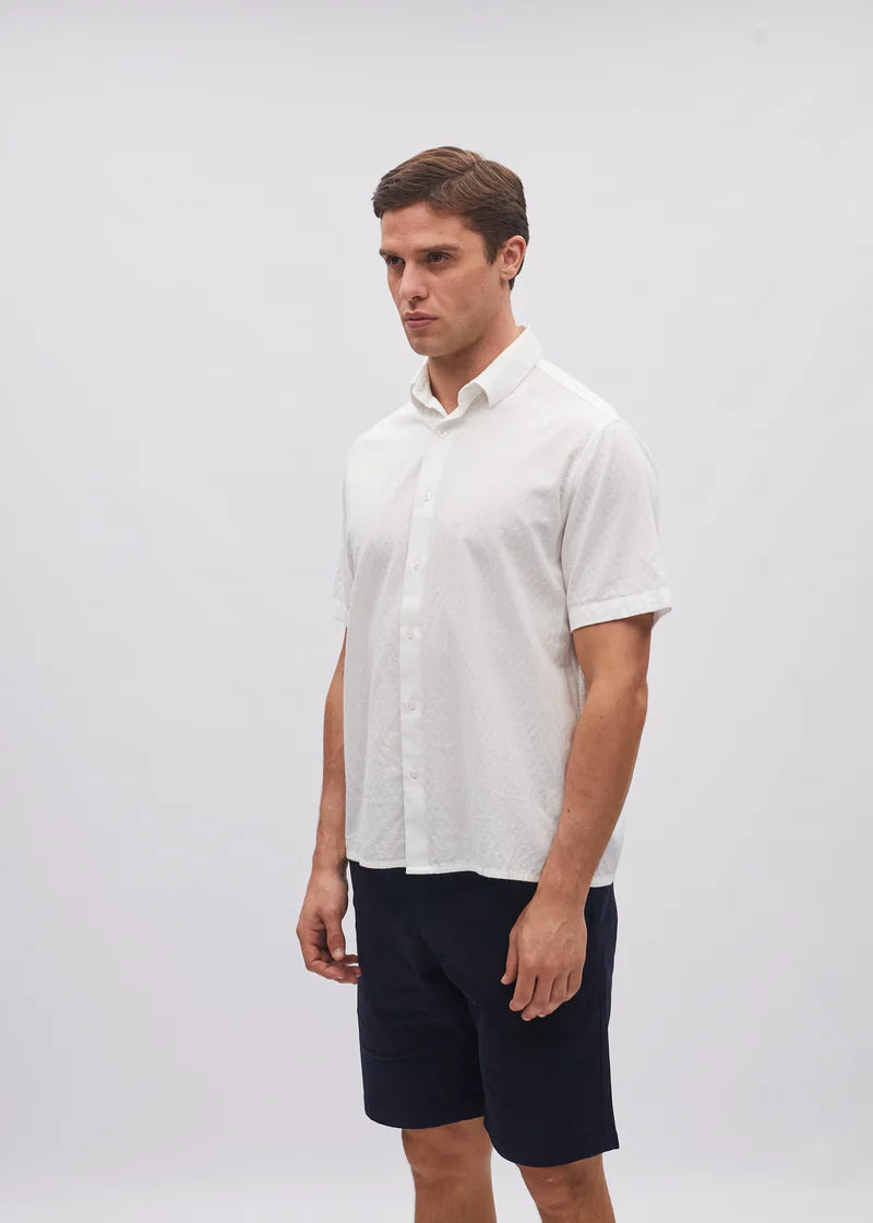 Man wearing a white shirt and navy shorts on a plain background