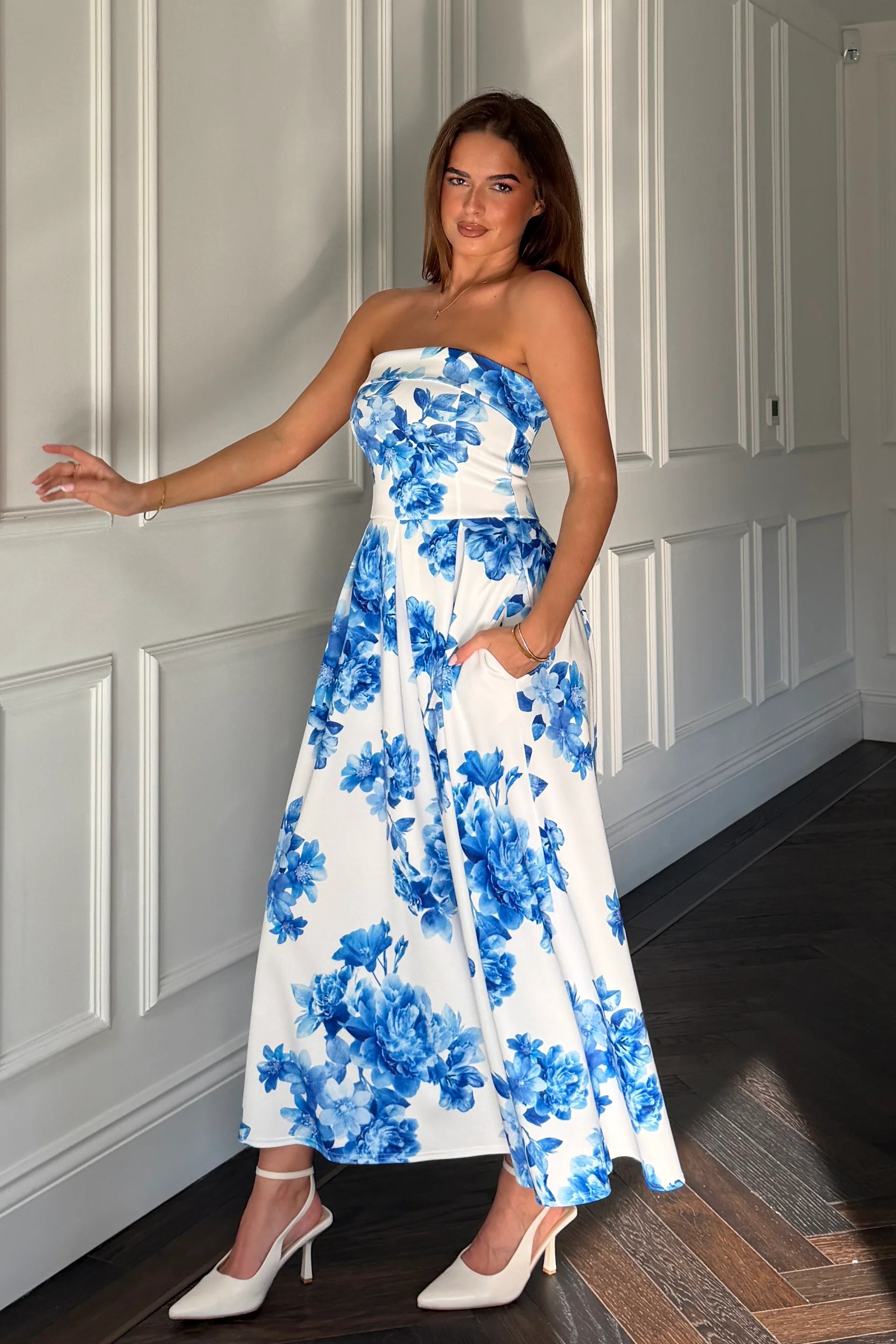 Woman wearing a strapless floral dress with blue flowers in a room with white paneled walls.