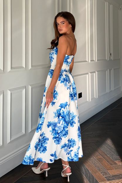Woman wearing a blue floral dress standing against a white paneled wall.