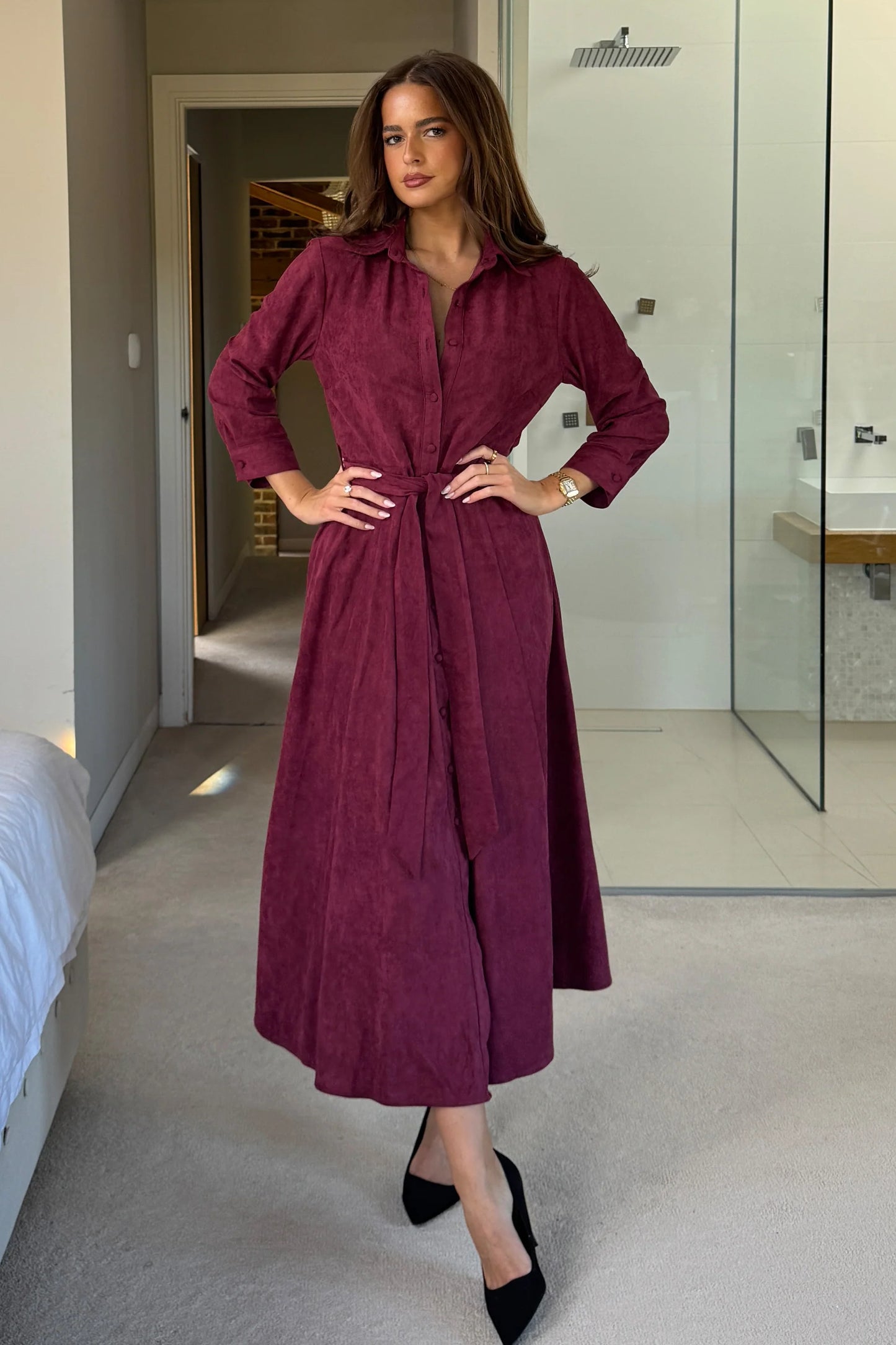 Woman in a long burgundy dress standing in a modern interior setting.