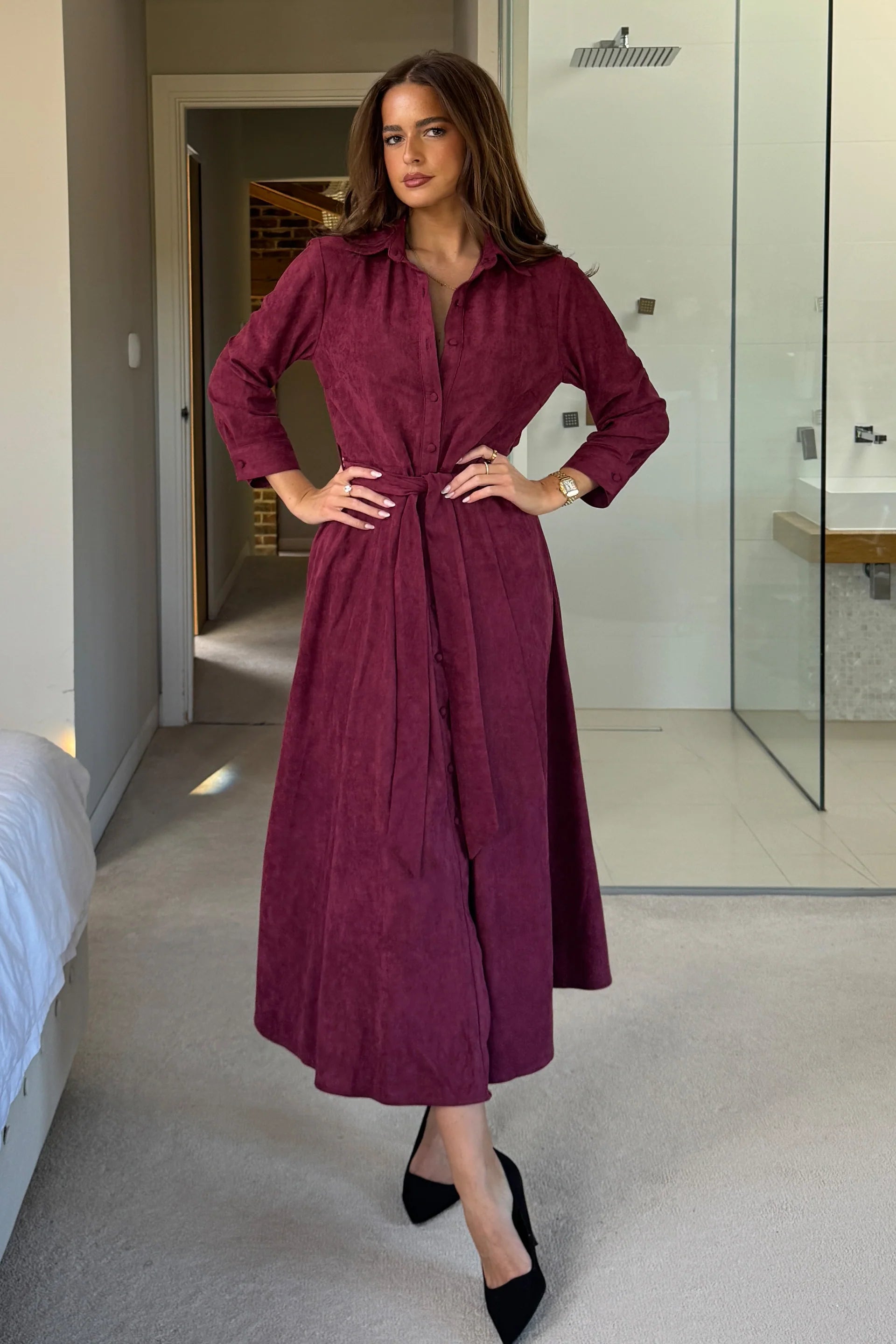 Woman in a long burgundy dress standing in a modern interior setting.