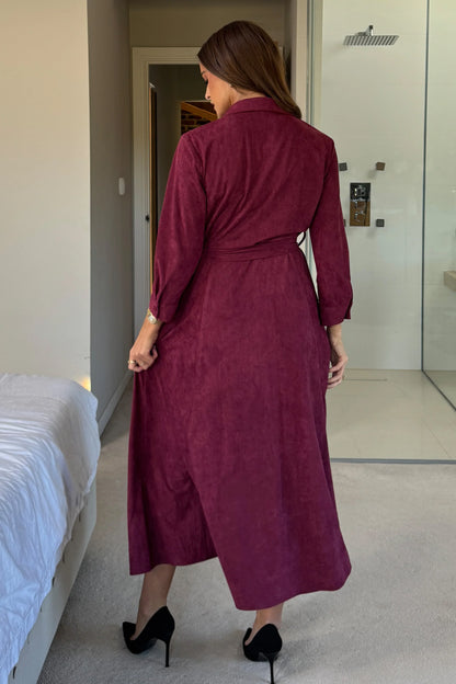 Woman wearing a burgundy dress standing in a bedroom.