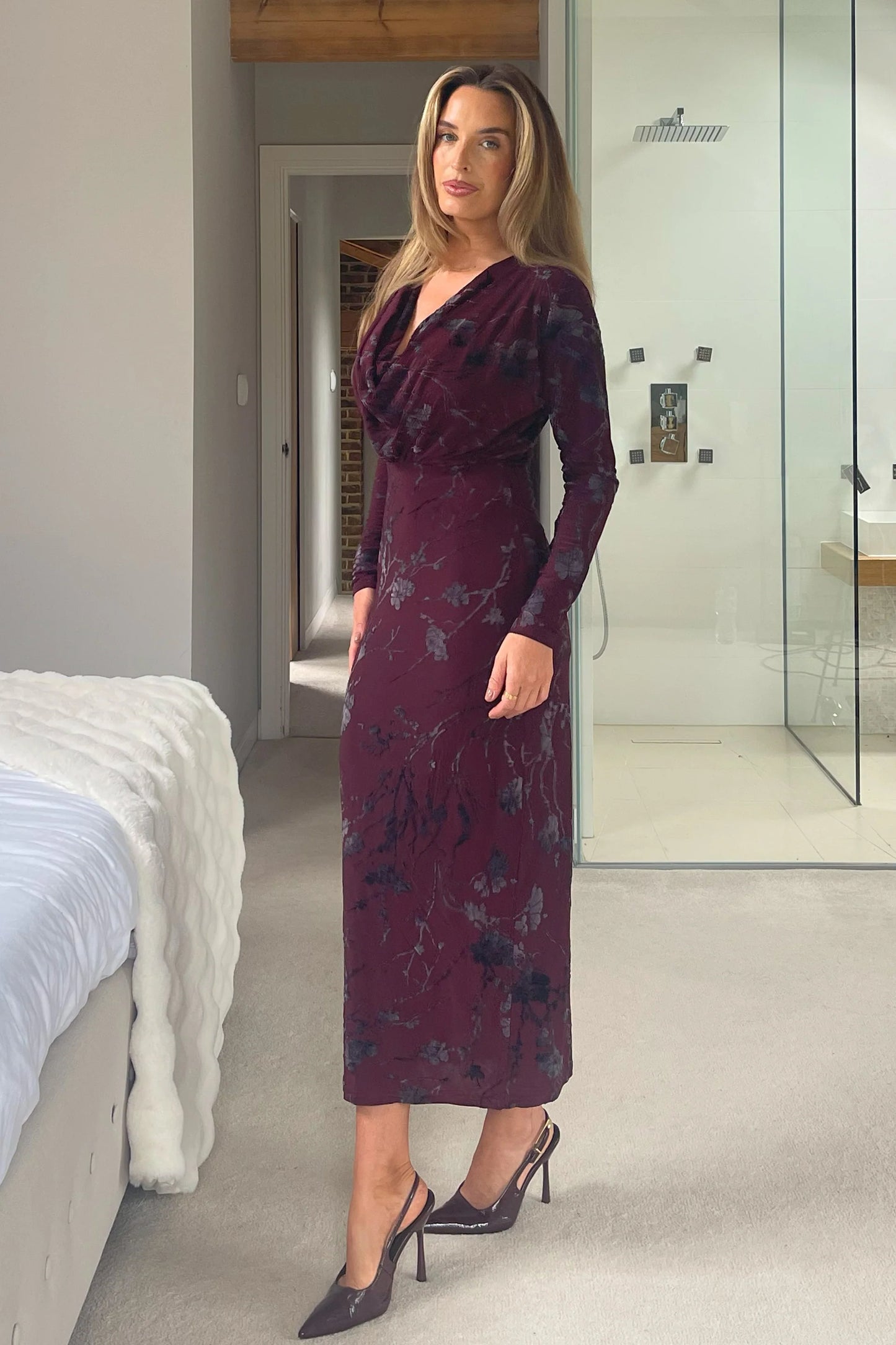 Woman wearing a dark purple floral dress in a modern room.