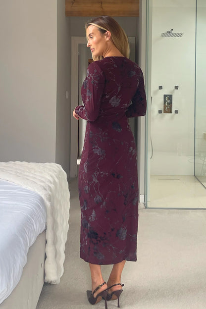 Woman in a burgundy patterned dress standing in a modern bedroom.