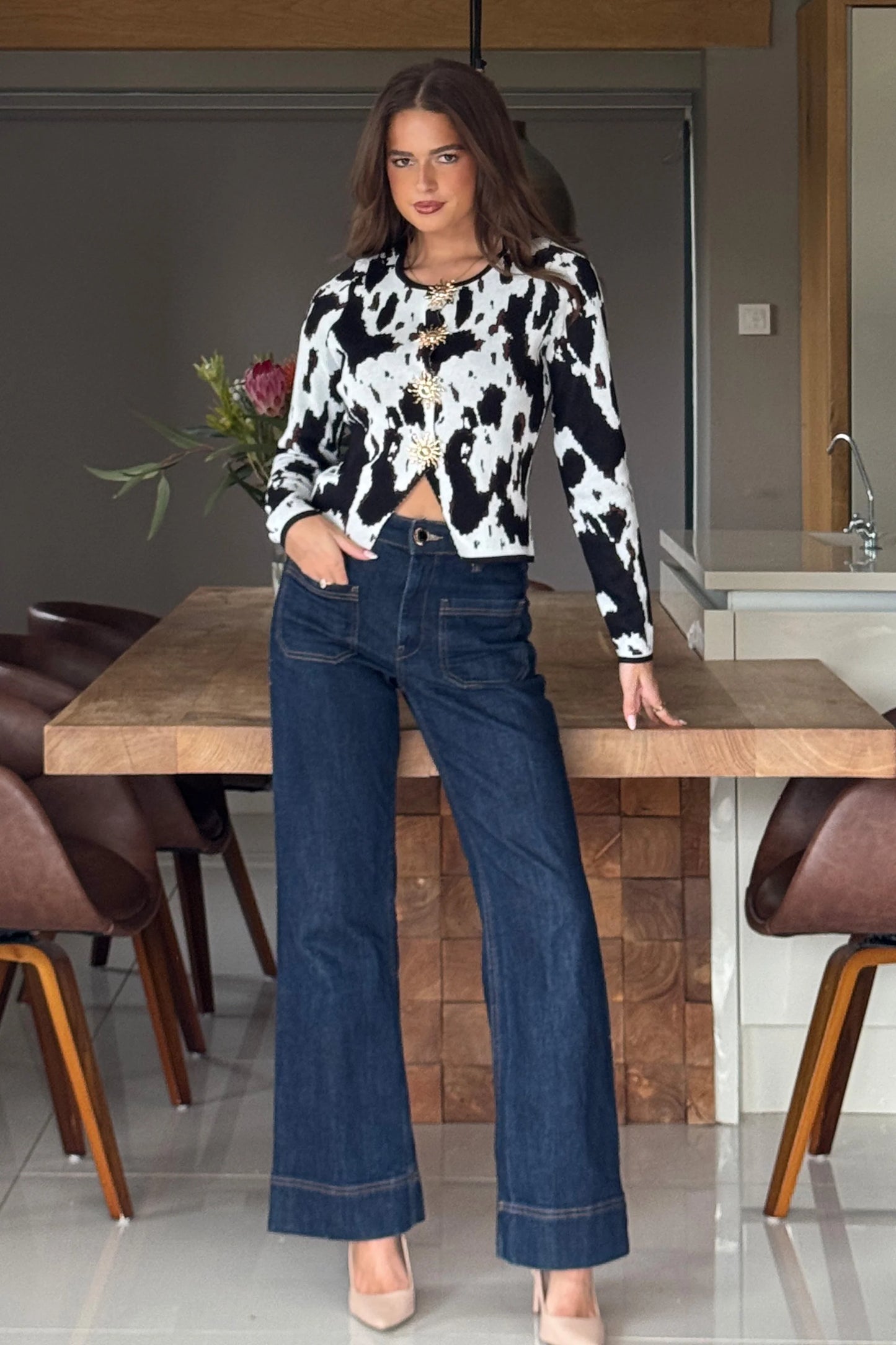 Woman in a cow print top and blue jeans standing in a kitchen.