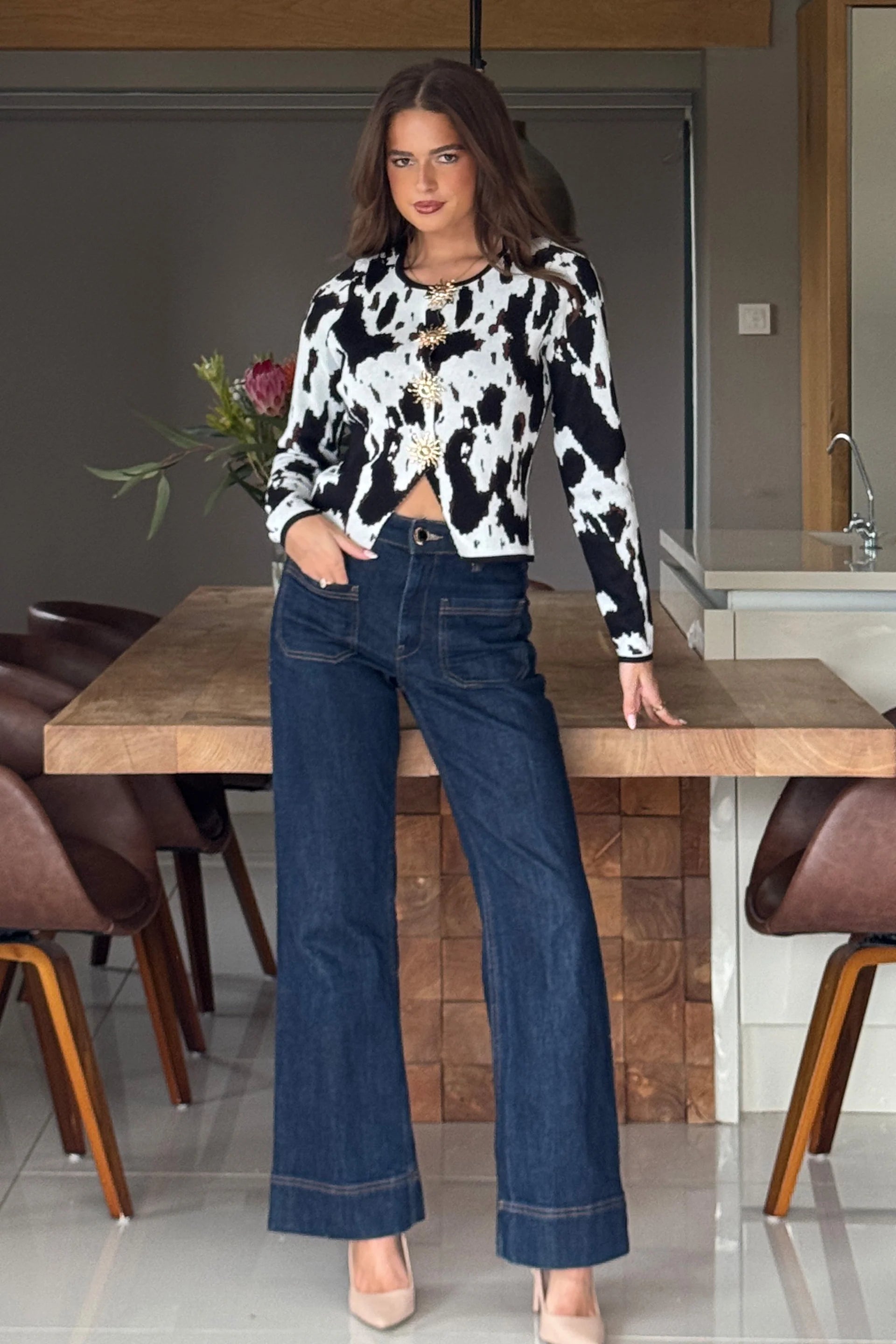 Woman in a cow print top and blue jeans standing in a kitchen.