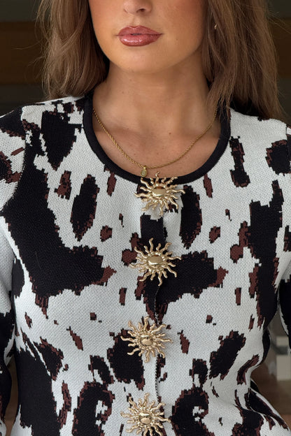 Person wearing a patterned top with gold sun-shaped brooches and a blurred background