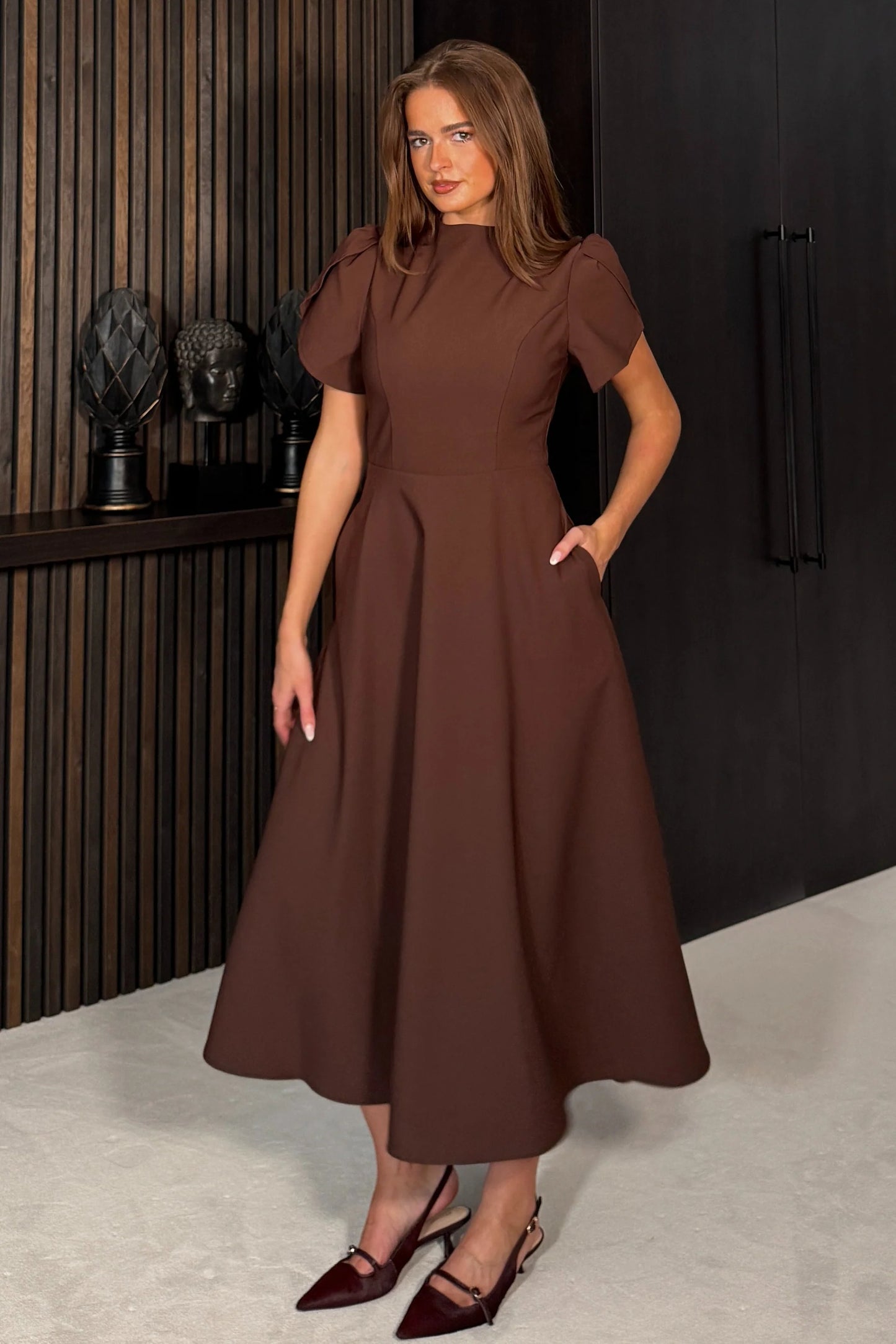 Woman wearing a brown dress standing in an indoor setting.