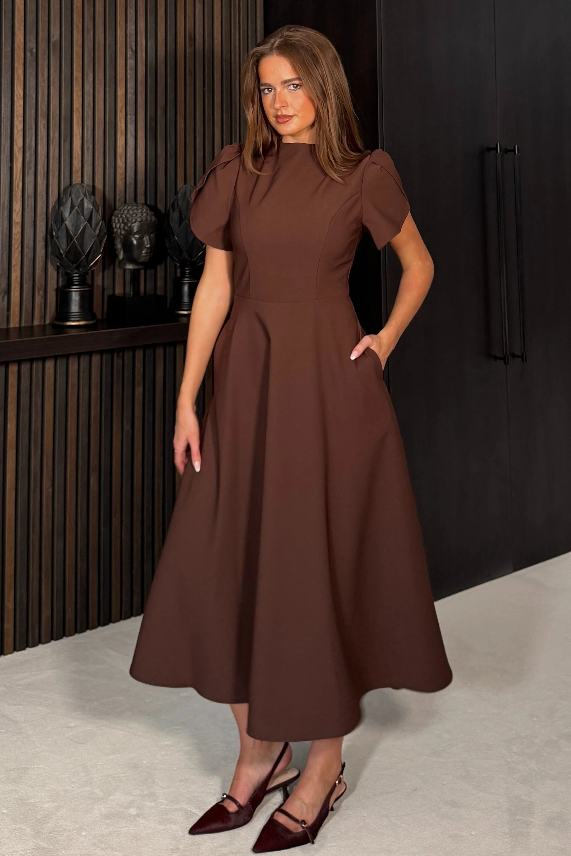 Woman wearing a brown dress standing in an indoor setting.
