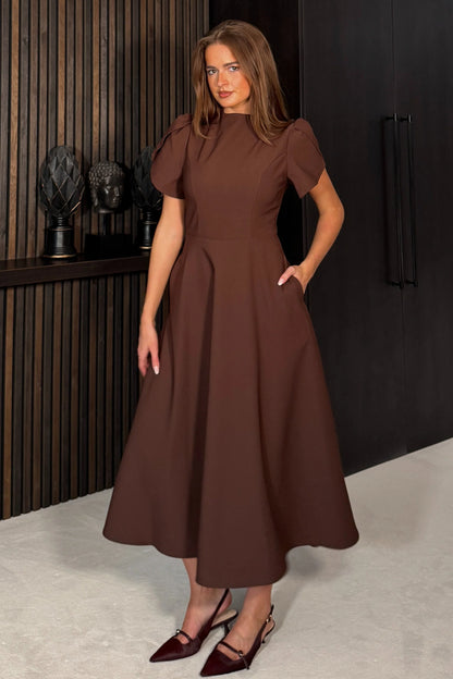 Woman wearing a brown dress standing in an indoor setting.