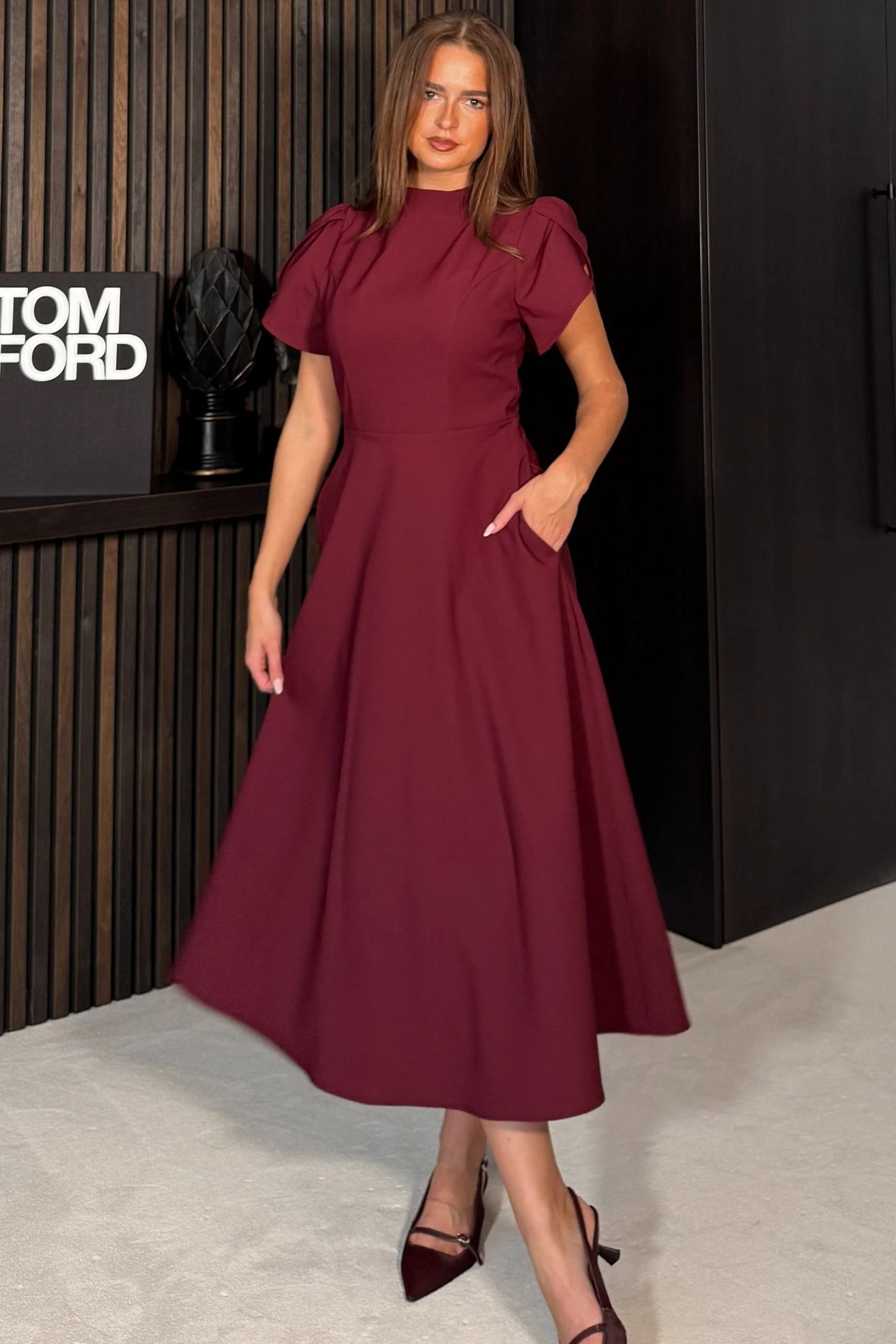 Woman in a burgundy dress standing in front of a Tom Ford display.