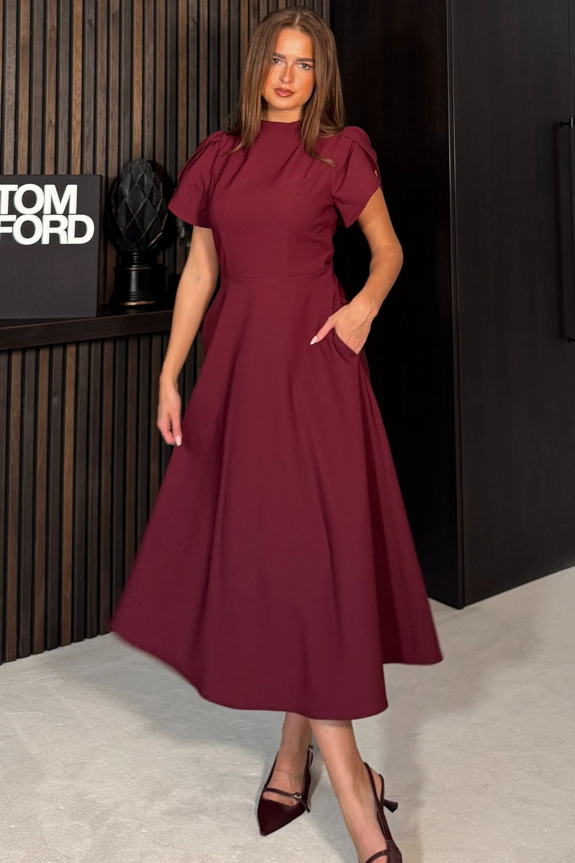 Woman in a burgundy dress standing in front of a Tom Ford display.