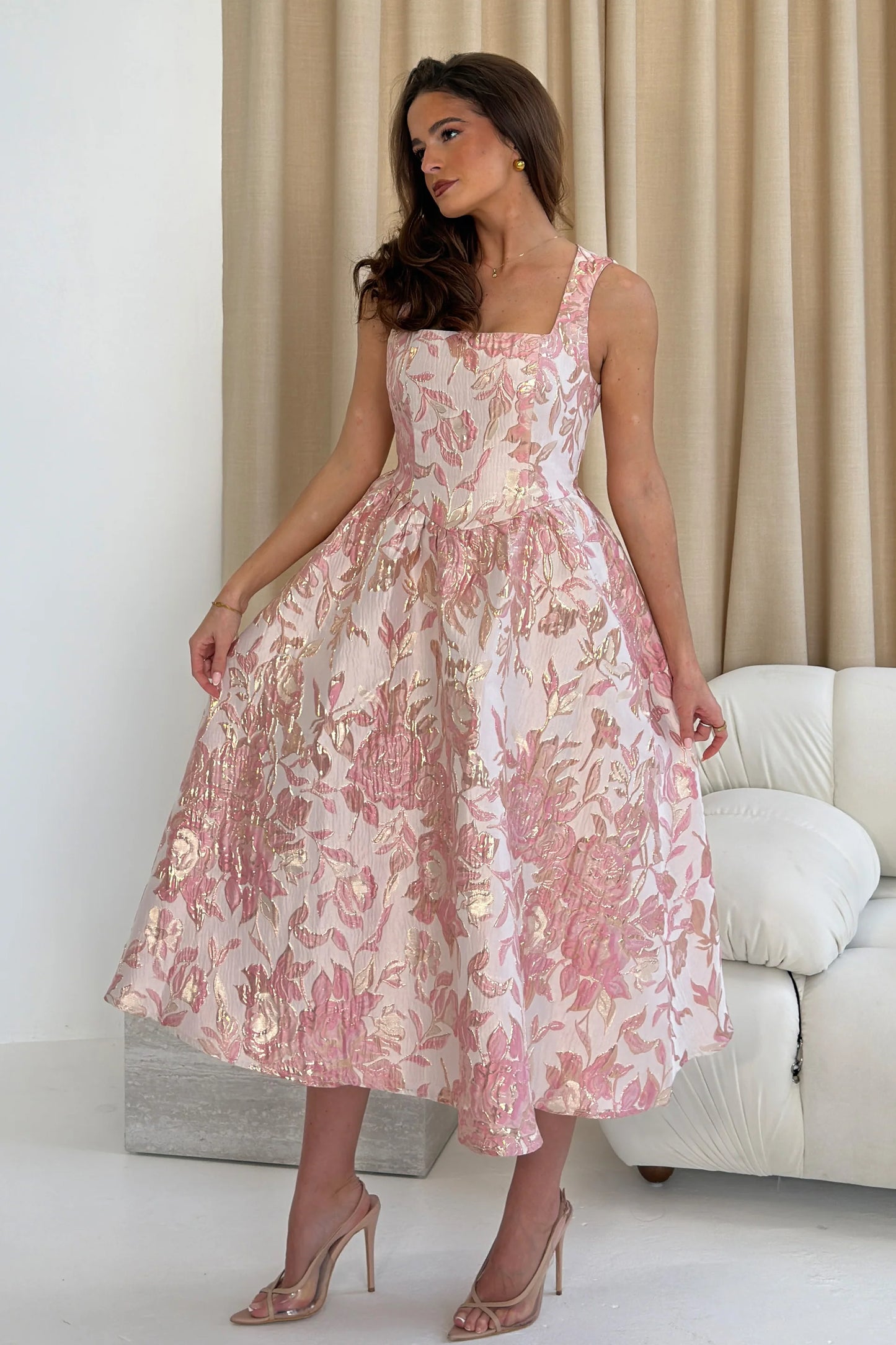 Woman wearing a pink floral dress in a minimalistic room.