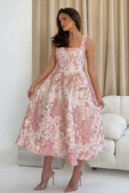 Woman wearing a pink floral dress in a minimalistic room.
