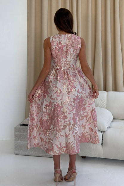 Woman in a floral dress standing in a living room with beige curtains and a white sofa.