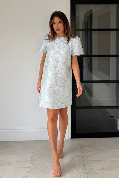 Woman wearing a light blue floral dress standing indoors.