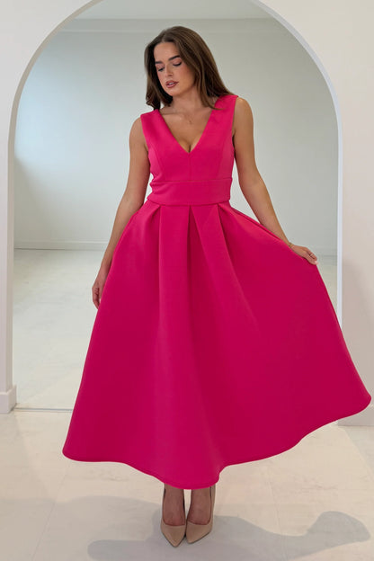 Woman wearing a bright pink dress standing in a well-lit room with an archway.