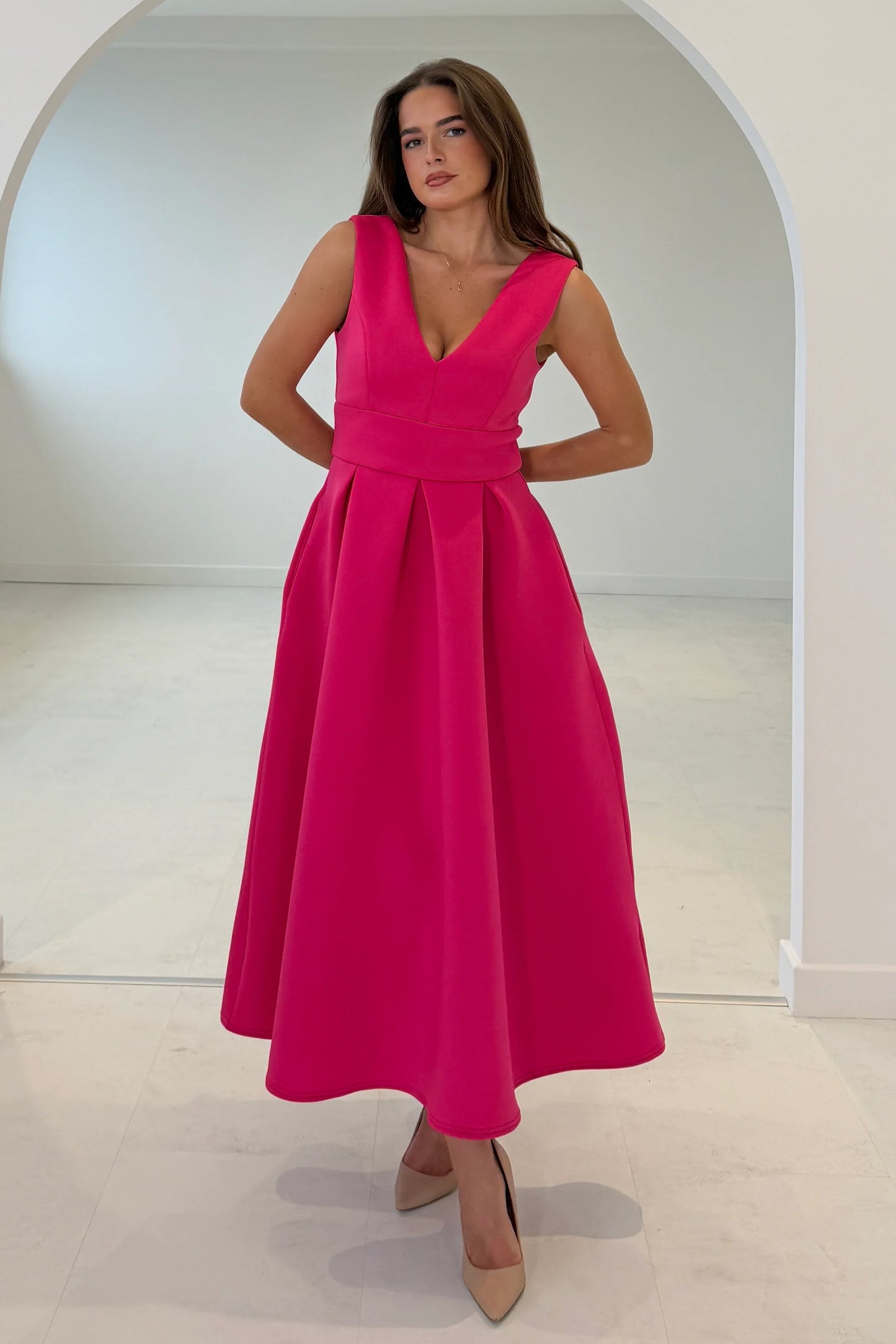 Woman wearing a bright pink dress standing in a minimalistic room.