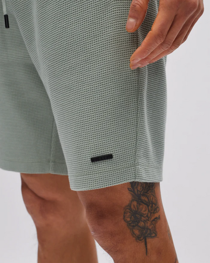 Close-up of a person wearing light gray shorts with a subtle pattern on a plain background.